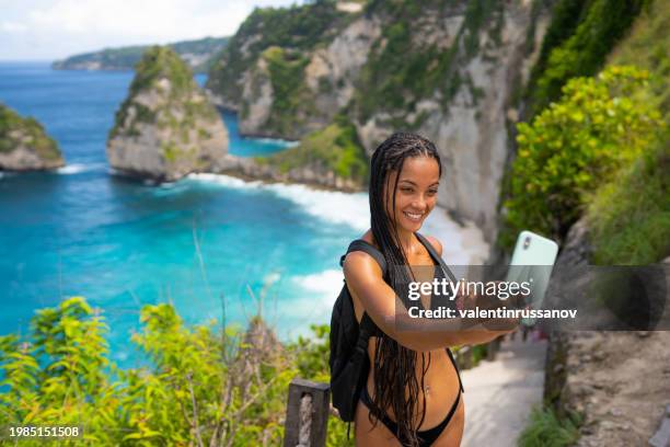 young female tourist in swimsuit taking selfie on kelingking beach on nusa penida island, bali, indonesia - animal waving stock pictures, royalty-free photos & images