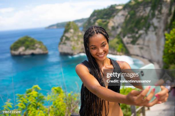 young female tourist in swimsuit taking selfie on kelingking beach on nusa penida island, bali, indonesia - animal waving stock pictures, royalty-free photos & images