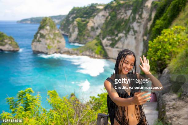 young female tourist in swimsuit taking selfie on kelingking beach on nusa penida island, bali, indonesia - animal waving stock pictures, royalty-free photos & images