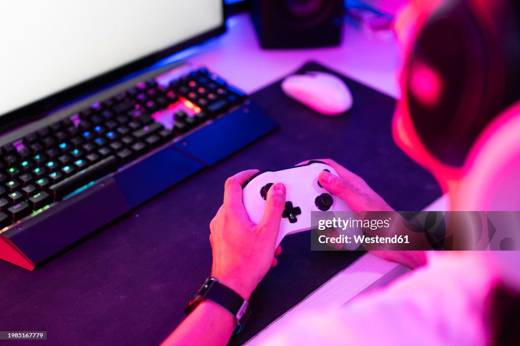 Gamer holding gamepad and playing video game on desktop