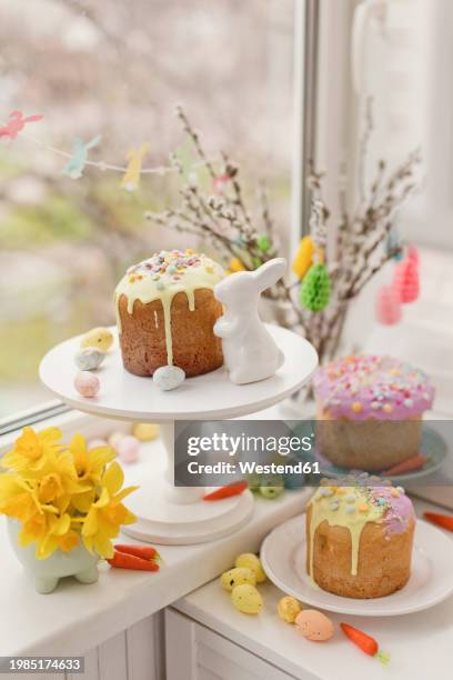 cakes decorated with flowers and eggs near easter bunny toy on window sill - adorno floral - fotografias e filmes do acervo