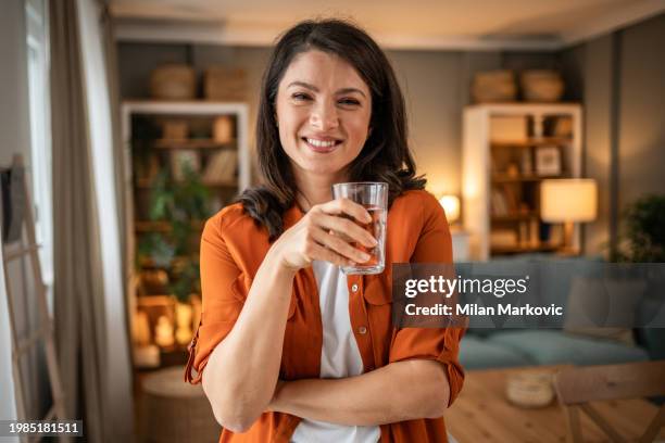 portrait of a smiling woman holding a glass of fresh clean drinking water. concept of healthy lifestyle and fluid intake - clean house stockfoto's en -beelden