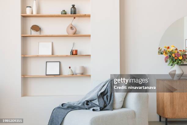 cosy armchair with a blanket in a living room next to shelves with assorted photo frames, vases and assorted ornaments - simple living room only stock pictures, royalty-free photos & images