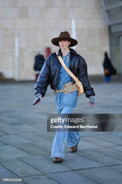Barbora Ondrackova wears a cowboy hat, a black oversized leather jacket, a blue denim ripped long top, blue flared denim jeans pants , brown leather...
