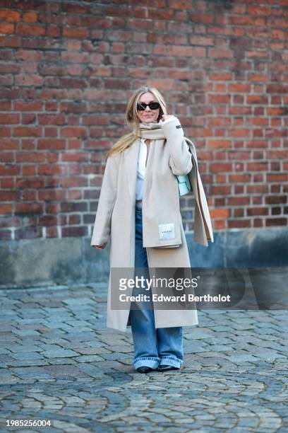 Guest wears sunglasses a scarf, a beige long coat , flared cuffed blue denim jeans pants , outside Herskind, during the Copenhagen Fashion Week AW24...