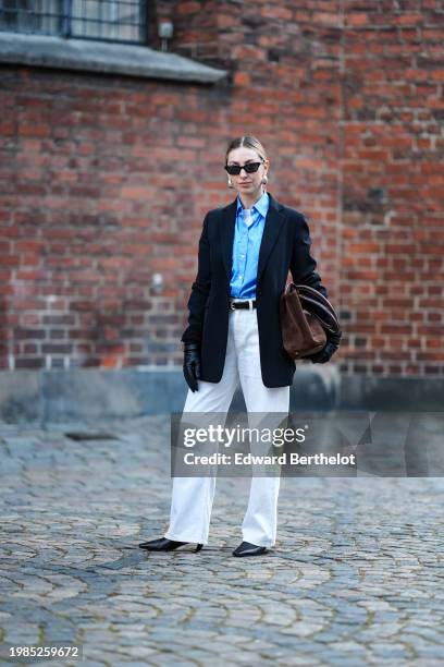 Guest wears sunglasses, earrings, a blue shirt, a black oversized blazer jacket , belt, a brown bag, white pants , black leather pointed shoes,...