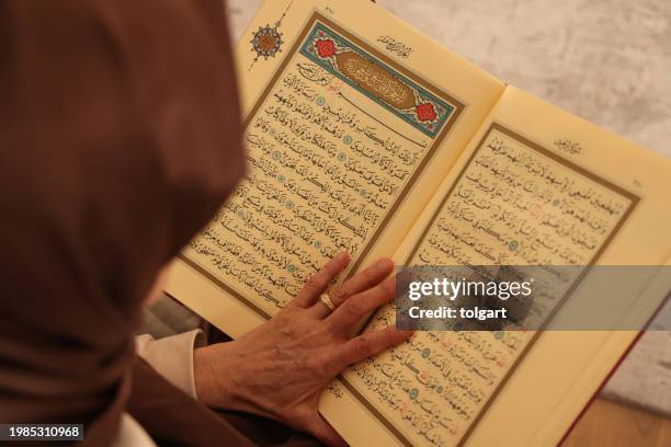 senior muslim woman reading quran at home - escritura árabe fotografías e imágenes de stock