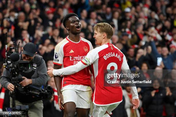 Bukayo Saka of Arsenal celebrates scoring his team's first goal with teammate Martin Odegaard during the Premier League match between Arsenal FC and...