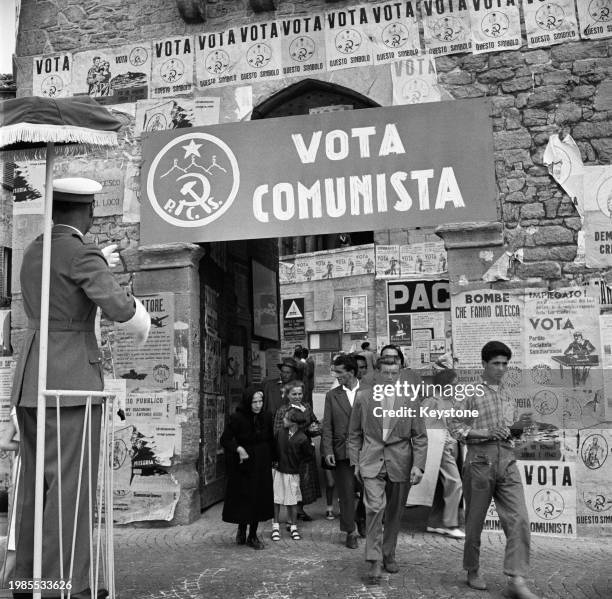 Traffic policeman on an elevated stand as Sammarinese people pass through an arched doorway, a pro-Sammarinese Communist Party sign across the...