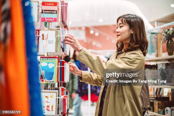 beautiful asian woman choosing & shopping for greeting cards in a gift shop - gift shop stock pictures, royalty-free photos & images