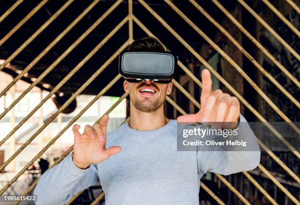 a young man in his mid-20s uses vr glasses and is visibly happy - simulator stock-fotos und bilder