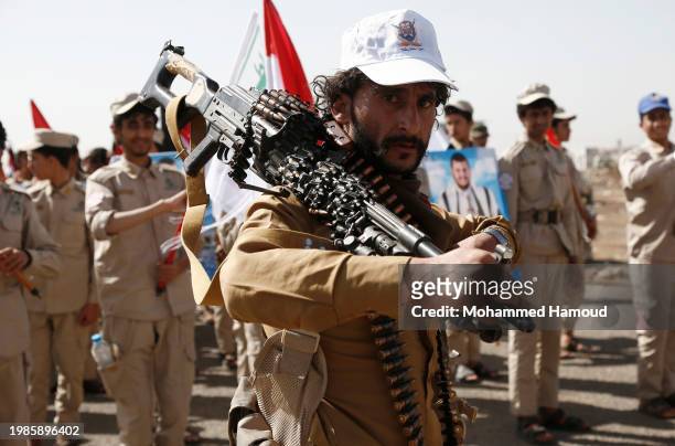 Houthi fighter carries a machine gun in front of scout team members carrying Yemeni and Palestinian flags, placards depicting Yemen's Houthi leader...