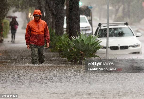 Person walks along a flooded street as a powerful long-duration atmospheric river storm, the second in less than a week, impacts California on...