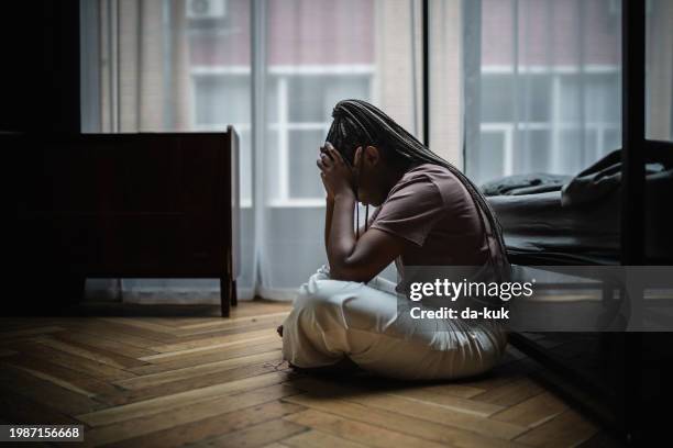 moment of depression, loneliness and emotional stress. young black woman sits on the floor near bed and looks very upset and stressed - histeria imagens e fotografias de stock