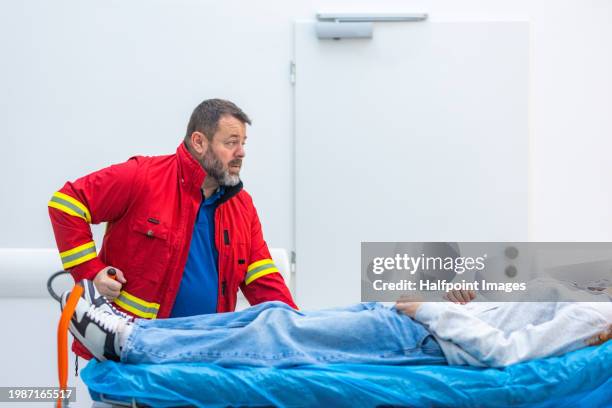 portrait of male paramedic pushing patient on stretcher across hospital corridor to emergency room. - acute care stock pictures, royalty-free photos & images
