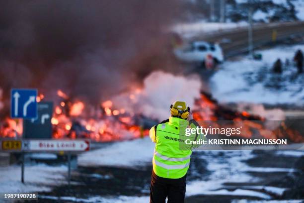 Road agency staff takes a picture as molten lava is seen overflowing the road leading to the famous tourist destination "Blue Lagoon" near Grindavik,...