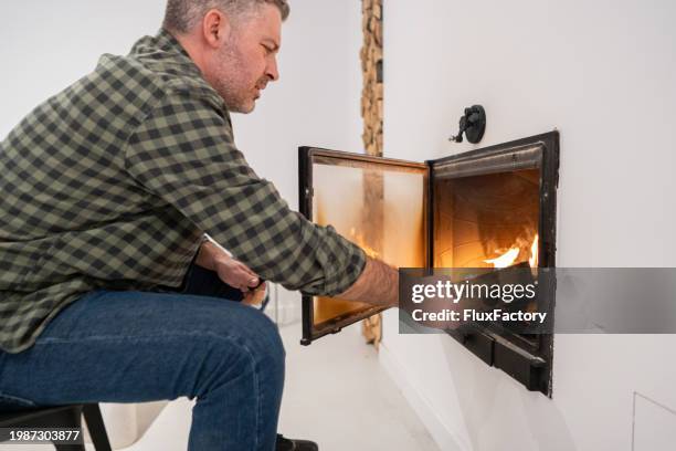 caucasian man put an log into fireplace, at his home - inserting stock pictures, royalty-free photos & images
