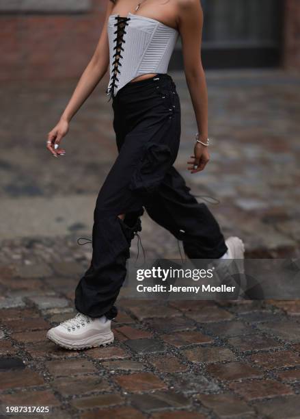 Madina Katter seen wearing silver necklaces, white / black corset top, black nylon cargo pants, white cotton socks and Hoka Tor Summit oat milk /...