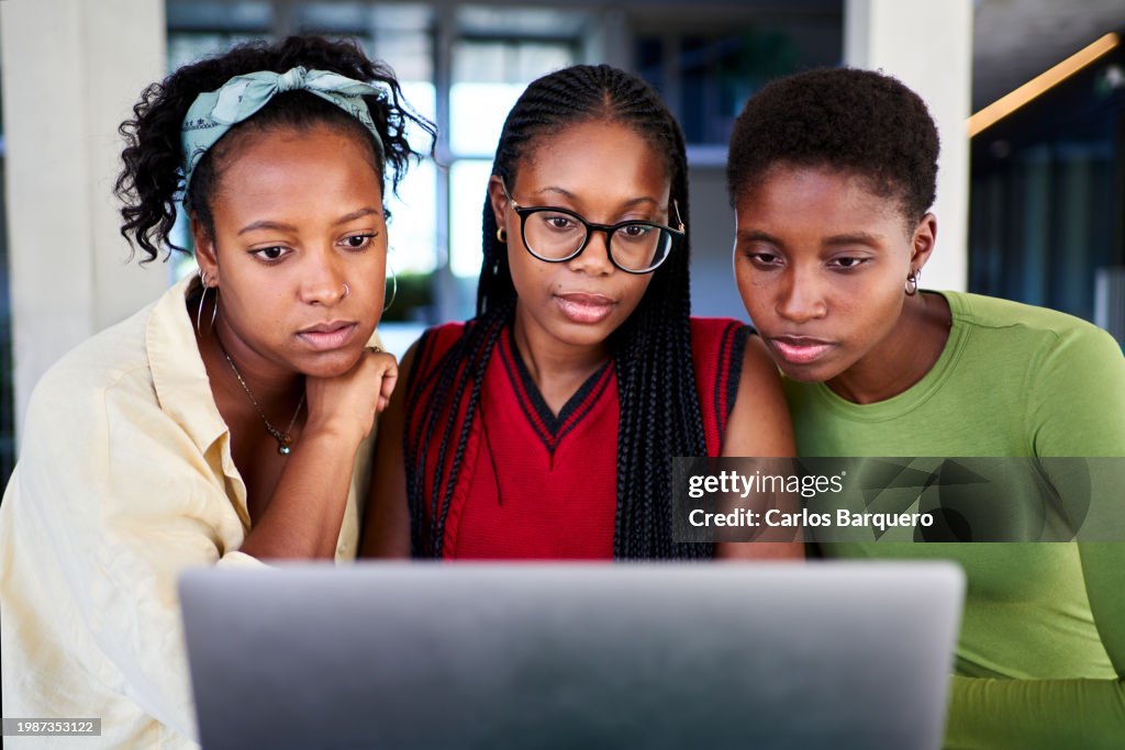 Three African-American students concentrated using a laptop computer to do homework together on the university campus.