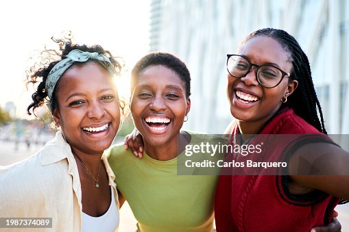 Portrait of three cheerful African-American women friends looking at the camera with big smiles, having fun together outdoors in the city.