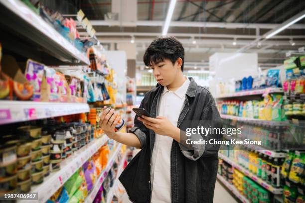 asian chinese student looking at smartphone while choosing items in supermarket. - etiqueta nutricional imagens e fotografias de stock