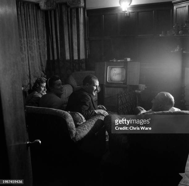 British racing driver Stirling Moss chatting with his father Alfred Moss as they watch TV with his sister Pat Moss and a friend, Sally Hindmarsh, at...