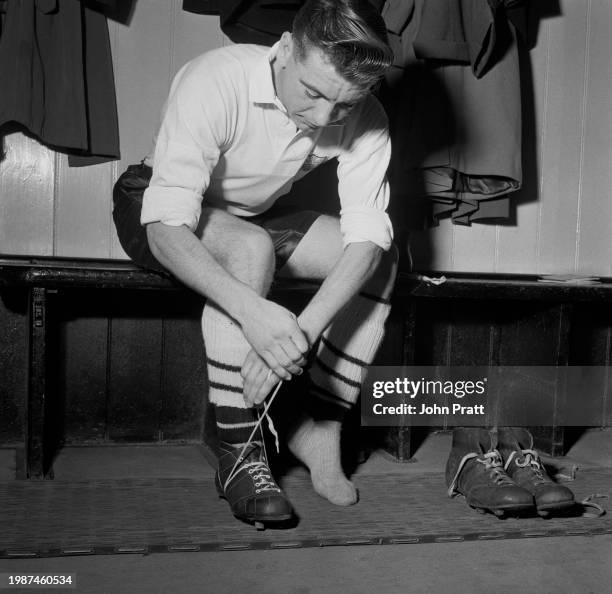 English footballer Johnny Haynes , an inside forward with Fulham FC, putting on his football boots in the changing room at Craven Cottage stadium in...