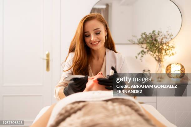 estetista sorridente durante l'esecuzione del trattamento di fototerapia - estetista foto e immagini stock