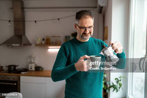 caucasian man pouring coffee from moka pot into mug - moka pot stockfoto's en -beelden