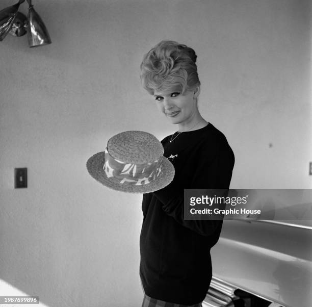 American actress and singer Connie Stevens, wearing a black crew neck top, poses holding a straw boater, United States, circa 1965.