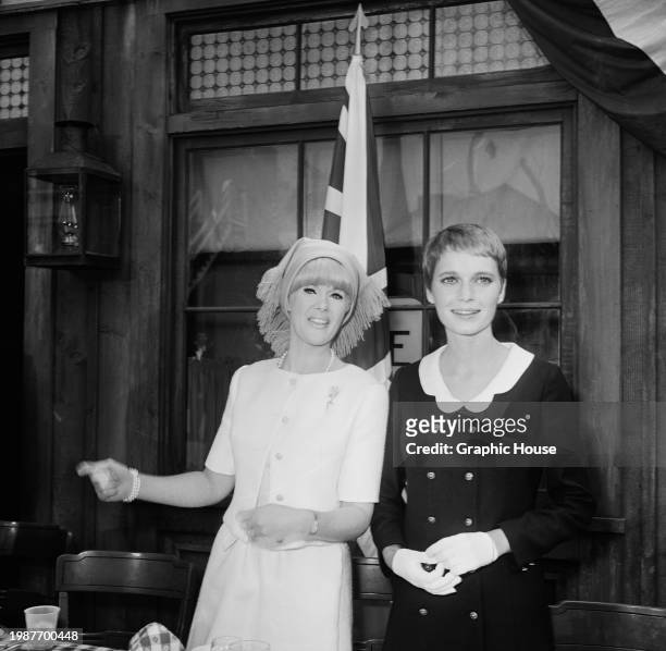 American actress Connie Stevens, wearing a white short-sleeved button-front top with a fringed hat, and American actress Mia Farrow, who wears a dark...
