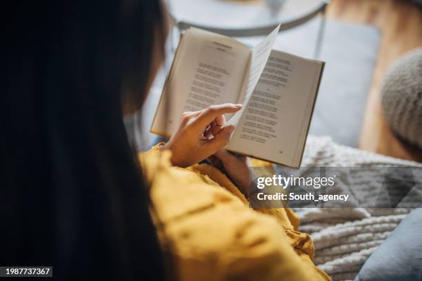 over the shoulder view of a young japanese woman reading a book on the sofa. - reading paper over shoulder stock pictures, royalty-free photos & images