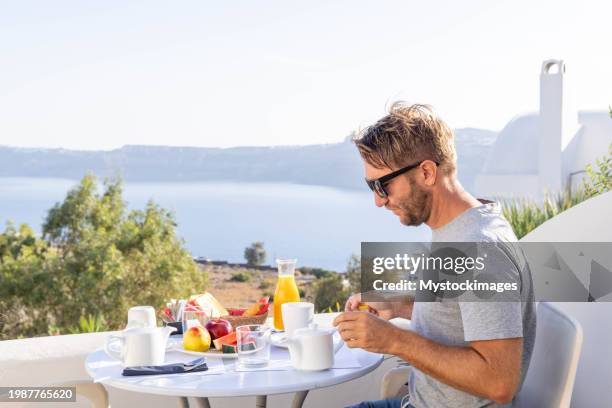 ägäischer genuss: junger mann genießt ein malerisches frühstück auf einer sonnigen terrasse in seiner privatvilla - private terrace balcony stock-fotos und bilder