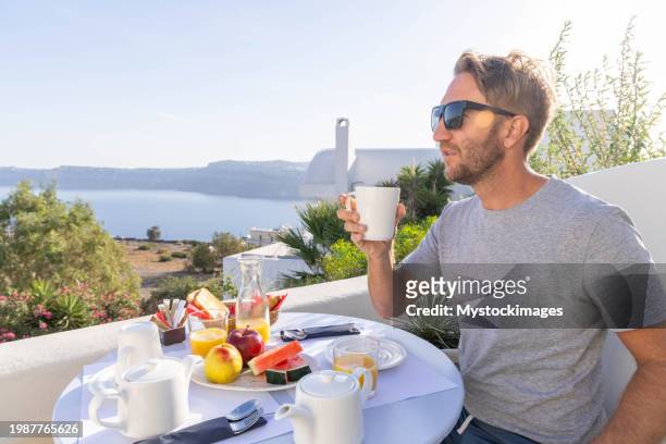 aegean delight: young man savors a scenic breakfast on a sunny terrace in his private villa - private terrace balcony stock pictures, royalty-free photos & images