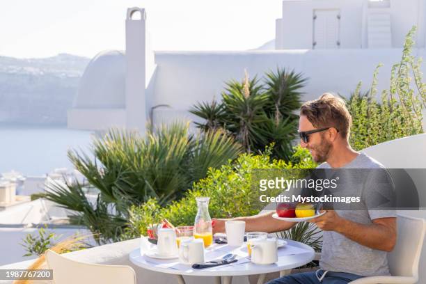 aegean delight: young man savors a scenic breakfast on a sunny terrace in his private villa - private terrace balcony stockfoto's en -beelden