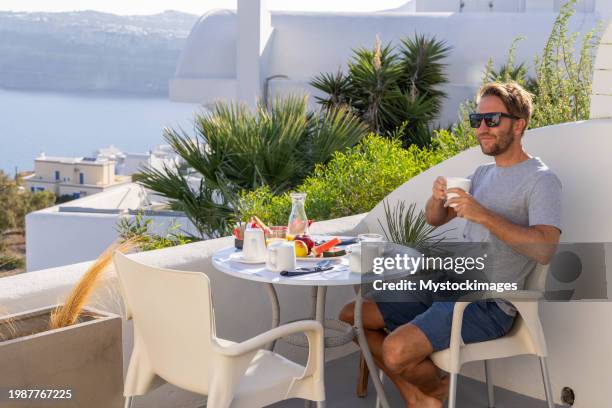 aegean delight: young man savors a scenic breakfast on a sunny terrace in his private villa - private terrace balcony stock-fotos und bilder