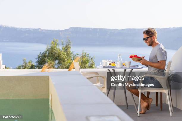 aegean delight: young man savors a scenic breakfast on a sunny terrace in his private villa - private terrace balcony stock pictures, royalty-free photos & images