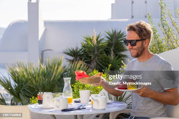 aegean delight: young man savors a scenic breakfast on a sunny terrace in his private villa - private terrace balcony stock pictures, royalty-free photos & images