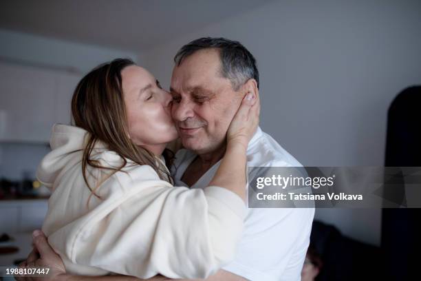 beautiful woman sharing loving hug and kiss with senior father embodying deep bond and care - reencuentro fotografías e imágenes de stock