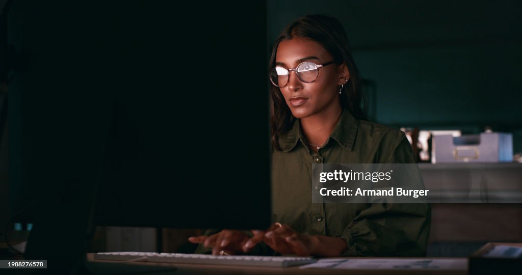Business woman, reading on computer and night research for information technology and software solution. Young programmer or developer with glasses, planning and typing on desktop in a dark office