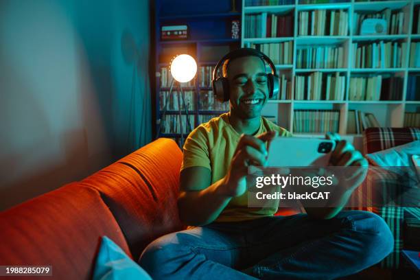 young man watching online content on smart phone at home - serviço de distribuição digital contínua imagens e fotografias de stock