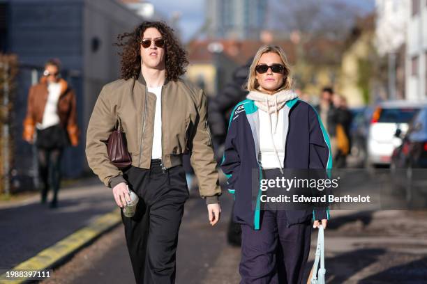 Pim Spoor wears sunglasses, a khaki bomber jacket , a brown leather bag, black pants ; guest wears sunglasses, a white wool balaclava, a navy blue...