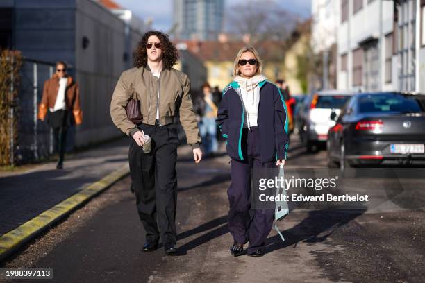 Pim Spoor wears sunglasses, a khaki bomber jacket , a brown leather bag, black pants ; guest wears sunglasses, a white wool balaclava, a navy blue...