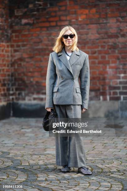 Guest wears sunglasses, a gray oversized blazer jacket , suit flared pants , shiny sequined shoes, a black woven leather Bottega Veneta bag, outside...