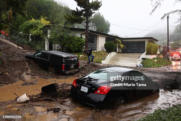 Person attempts to clear away debris from a mudslide as a powerful long-duration atmospheric river storm, the second in less than a week, continues...