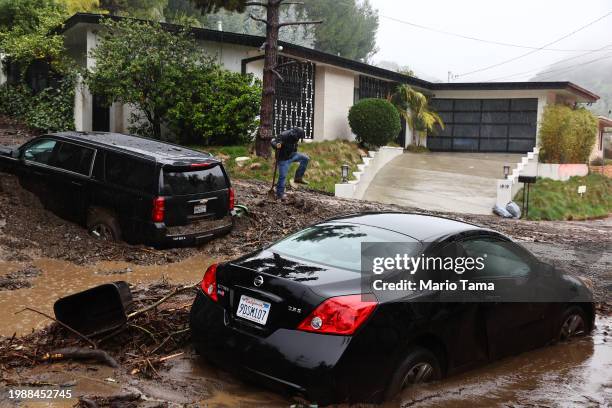 Person attempts to clear away debris from a mudslide as a powerful long-duration atmospheric river storm, the second in less than a week, continues...