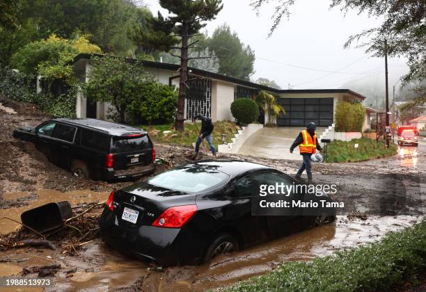 Person attempts to clear away debris from a mudslide as a powerful long-duration atmospheric river storm, the second in less than a week, continues...