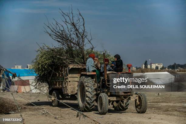 Displaced Syrians carry on a tractor tree branches to cut into twigs to be used for cooking, at the Al-Younani camp on the outskirts of the northern...