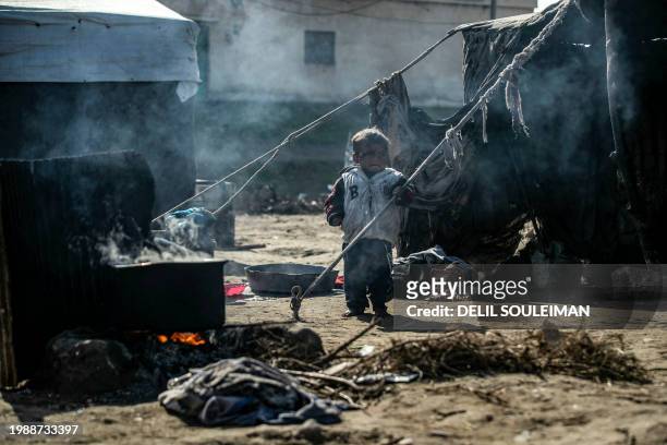 Displaced Syrian child stands near a makeshift stove using wood twigs for cooking, at the Al-Younani camp on the outskirts of the northern city of...