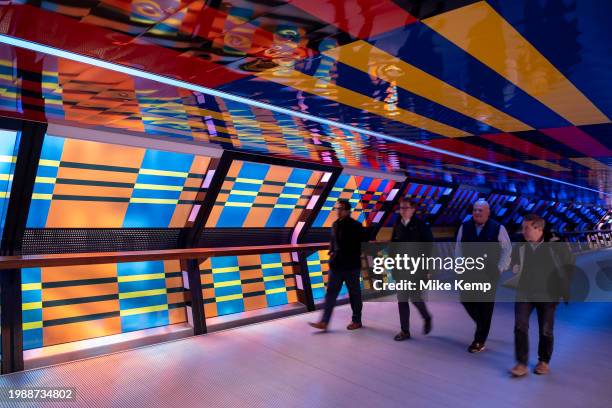 People interacting with the geometric public contemporary artwork 'Captivated by Colour' by artist Camille Walala in the tunnel walkway at Adams...